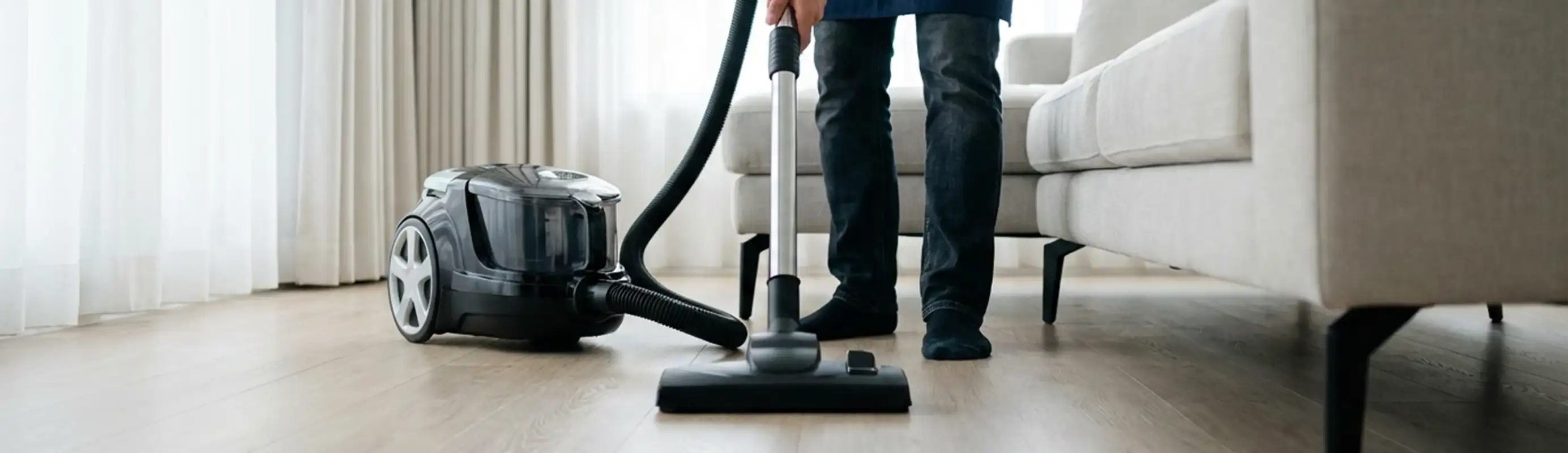 Professional house cleaner vacuuming a living room floor with a canister vacuum cleaner, Wilmington, NC.