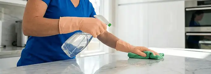Maid service worker spraying and wiping a kitchen countertop with a microfiber cloth for sanitizing, Wilmington, NC.