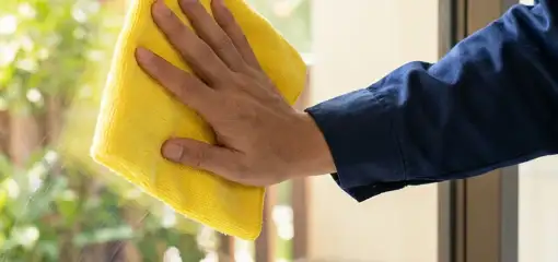 House cleaner wiping a glass window with a yellow microfiber cloth for streak-free cleaning, Wilmington, NC.